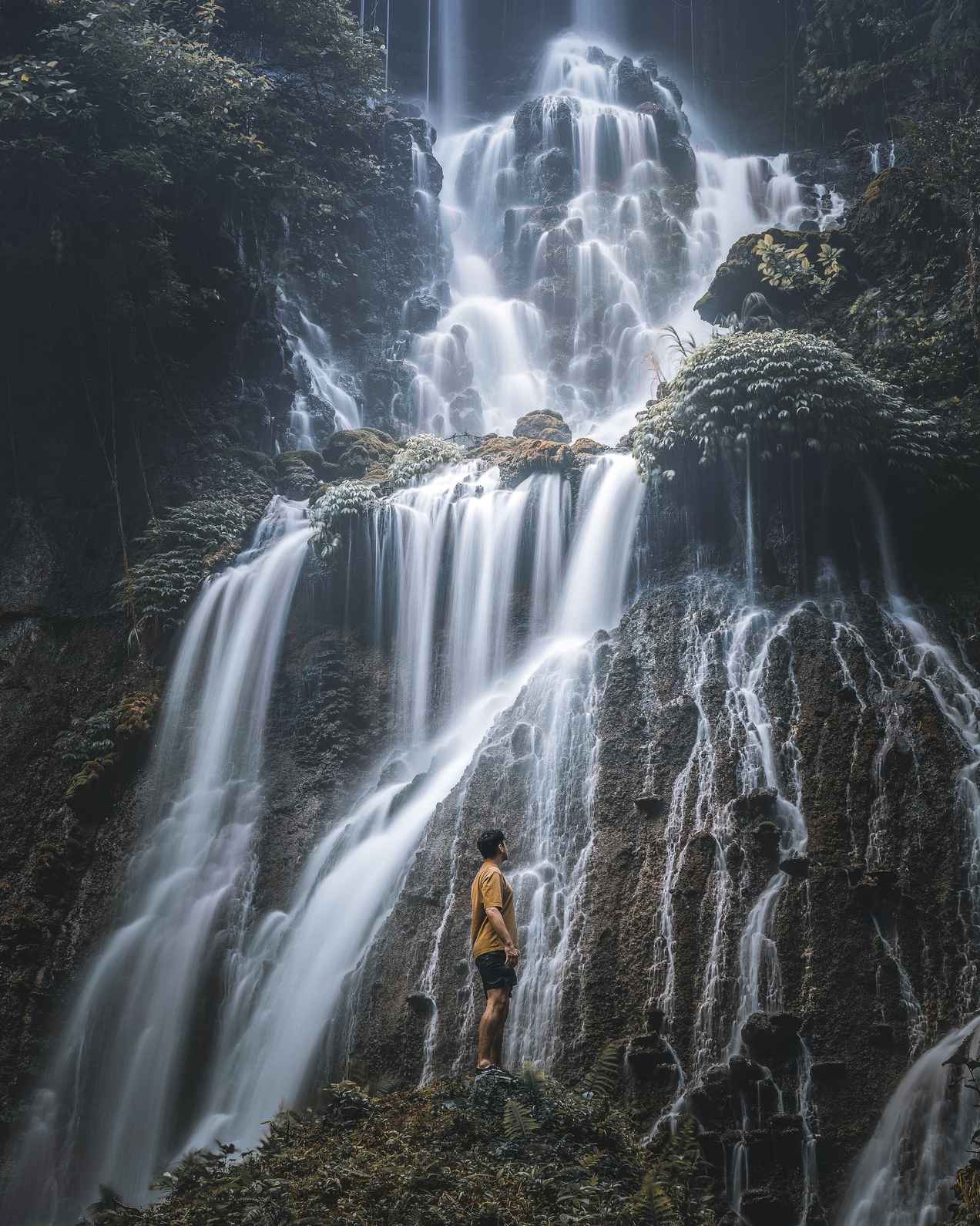 Person standing in front of the towering Tumpak Sewu Waterfall.