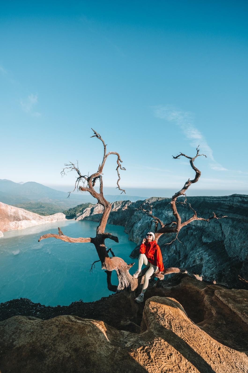 Traveler perched on a cliff with Ijen Crater's vibrant blue waters in the background.