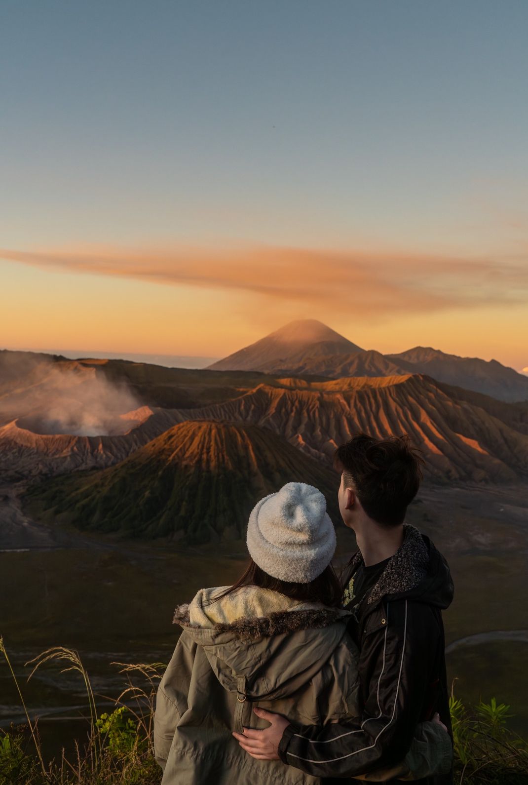 A couple standing and admiring the sunset at Mount Bromo, with the volcano in the background.