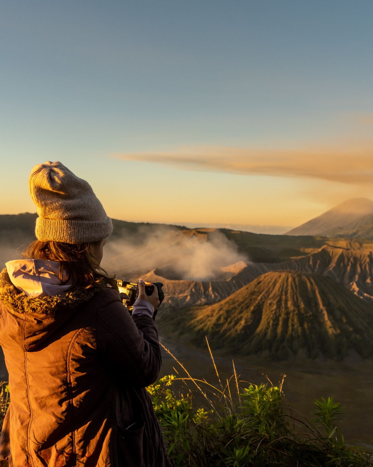 Tourist taking a photograph of Mount Bromo during sunrise, with the volcano in the background.