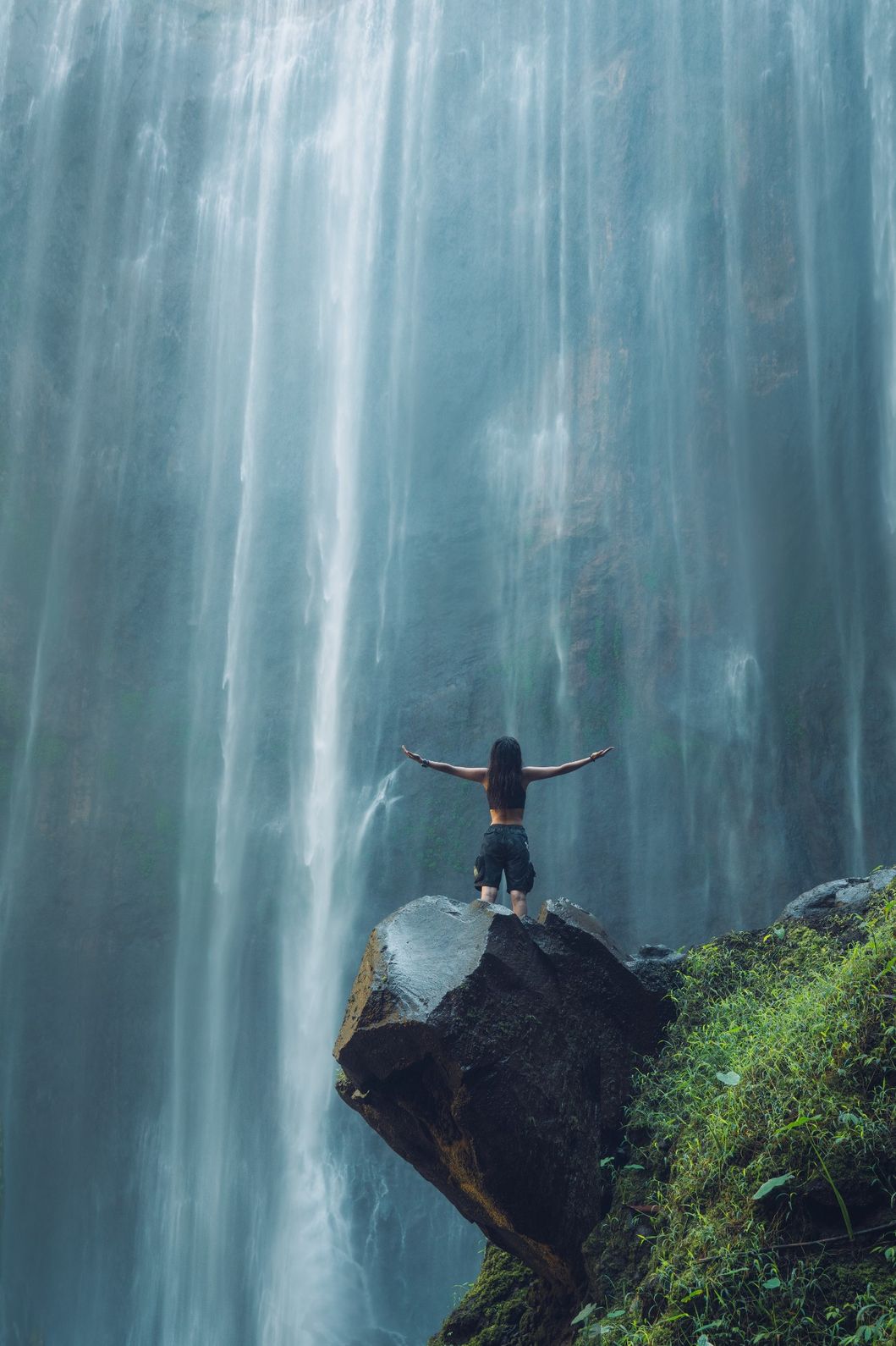 A visitor standing in front of the towering Tumpak Sewu Waterfall in East Java, Indonesia.