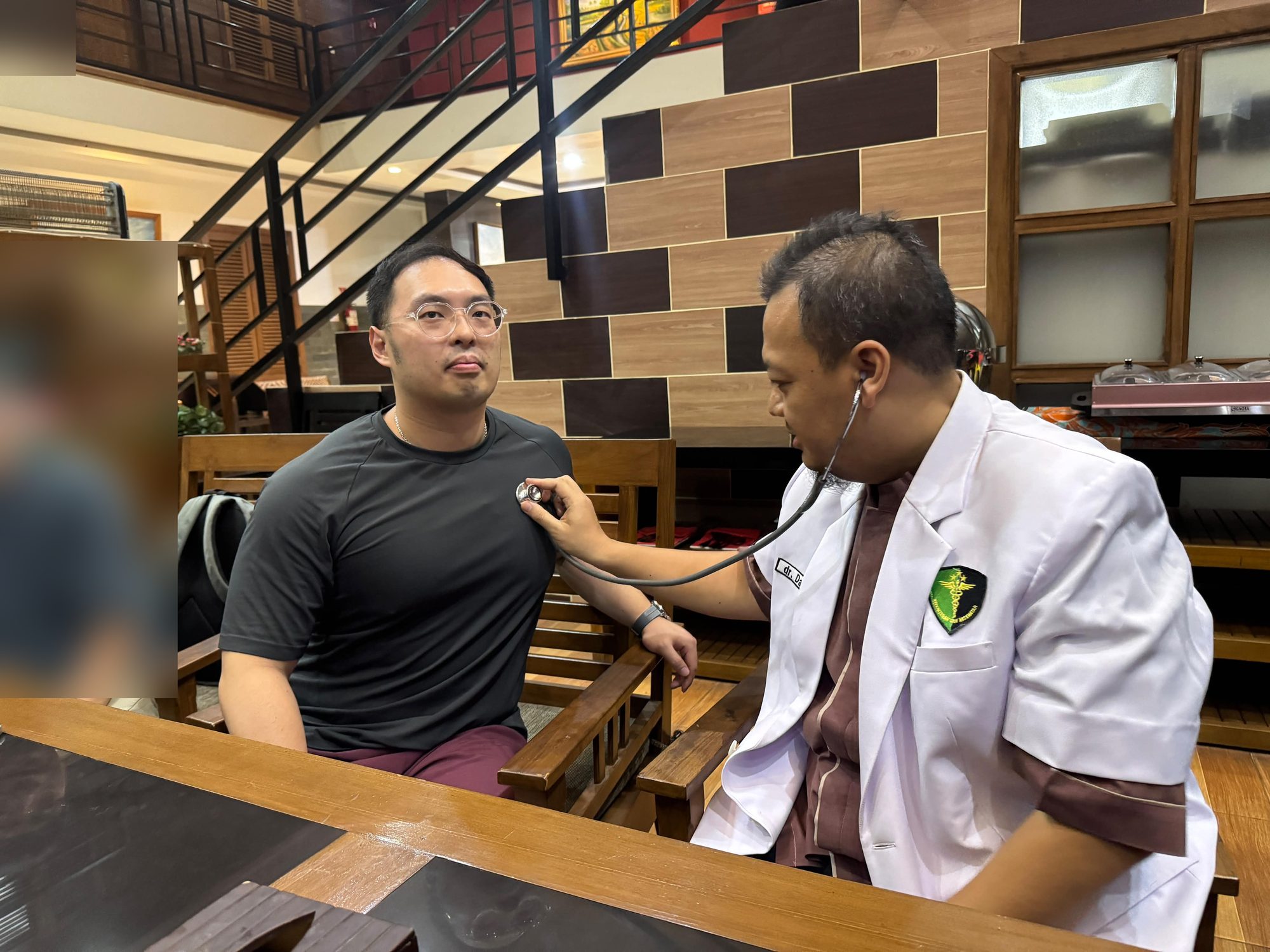 Preview: Dr. Ahmad Irwandanu examines a second guest's chest with a stethoscope during the Ijen pre-ascent health screening at Baratha Hotel, Bondowoso.